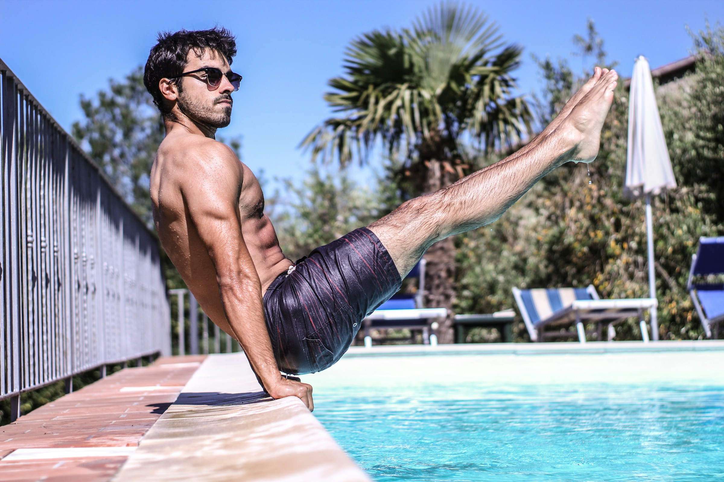 Sportlicher Mann mit dunklen Haaren macht ein Workout in Badehose am Pool